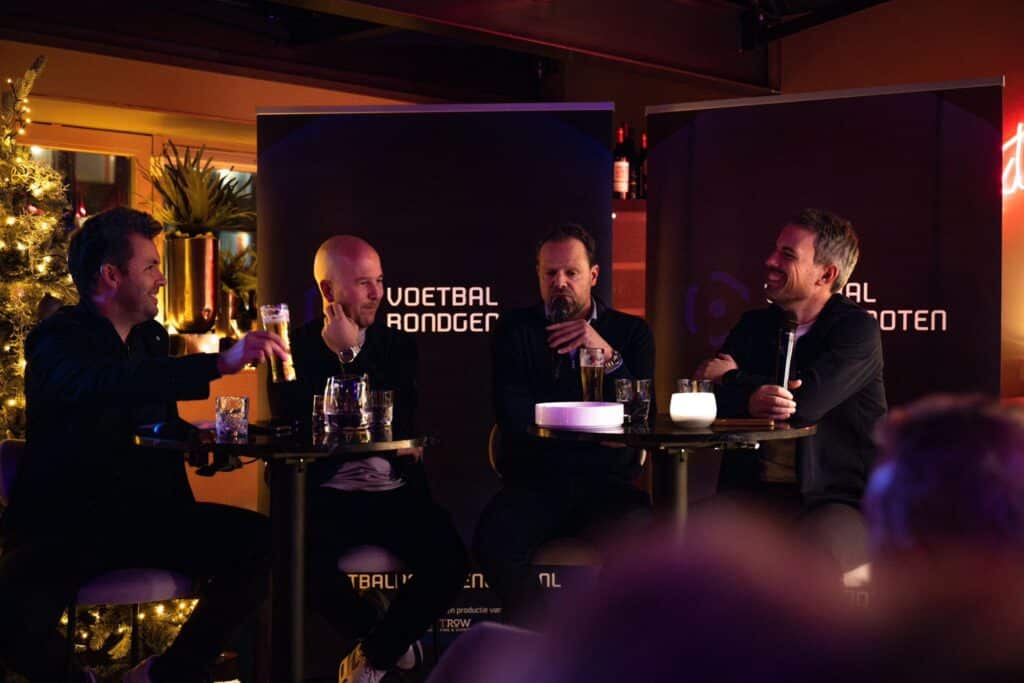 De vier organisatoren zitten aan een tafel met microfoon tijdens een business evenement georganiseerd door De Voetbalbondgenoten.