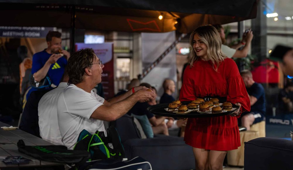 Een gastvrouw deelt tijdens een business event kleine hamburgertjes uit aan de deelnemers.