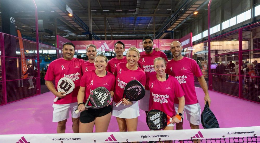 Een groep padelspelers in roze shirts poseert op een indoorbaan tijdens het Legends League Pink Ribbon-evenement, ter ondersteuning van de #pinkmovement campagne.